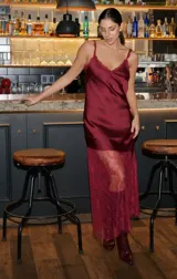 Vestido largo de seda color rojo, con escote en V y breteles finos. Presenta detalles de encaje en el escote y un diseño asimétrico en la falda que incorpora encaje transparente desde la altura de la rodilla.