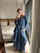 Pollera larga de jean fino color azul, con diseño amplio, elástico en la cintura y bolsillos delanteros grandes. Cuenta con pinzas y superposiciones de tela en los laterales que aportan volumen y movimiento.
