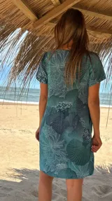 Vestido corto de lino color celeste con estampado de hojas y flores en tonos azules y blancos. Tiene cuello redondo, mangas cortas y bolsillos laterales.
