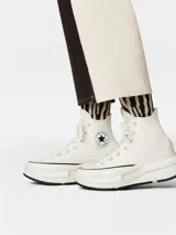 Championes Converse de caña alta con plataforma, confeccionados en lona de algodón. Presentan una mediasuela de espuma CX para mayor comodidad, puntera reforzada de goma con diseño distorsionado, zona del tobillo extragrande y lengüeta con alas para facilitar el calce.