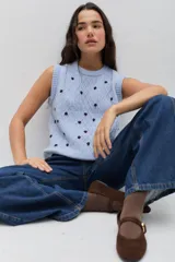 Chaleco de punto color celeste, con diseño de trenzas y pequeñas flores bordadas a mano en color marrón oscuro. Presenta cuello redondo y terminaciones acanaladas.