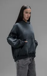 Hoodie oversize de corte crop en color gris oscuro con efecto desgastado. Presenta costuras expuestas, detalles de roturas en el ruedo y en la capucha, y bolsillos frontales con bordes reforzados.