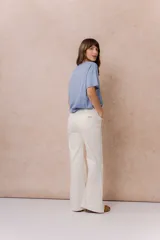 Pantalón jean de tiro alto y corte wide leg, color off white. Presenta un diseño minimalista con bolsillos funcionales, cierre frontal con botón y detalles metálicos plateados.