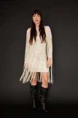 Vestido corto de manga larga confeccionado en tela con lentejuelas brillantes, caracterizado por sus largos flecos que caen desde los hombros hasta el ruedo. Presenta un corte ajustado al cuerpo y cuello redondo.