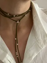 Corbatín tipo choker de tiento de gamuza color verde oliva, con detalle de pequeñas esferas metálicas plateadas distribuidas a lo largo de la tira.
