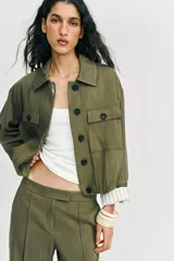 Chaqueta corta de color verde militar, con cuello solapa, bolsillos delanteros con solapa y cierre frontal de botones ocultos. Presenta mangas amplias con vuelta en los puños que muestran un forro a rayas.