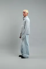 Polo de punto celeste con patrón trenzado, cuello tipo polo abierto y mangas largas. Presenta logos estampados en el pecho y diseño de estilo deportivo retro.