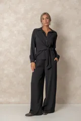 Camisa de corte clásico con cuello camisero, mangas largas con puños abotonados y cierre frontal con botones. Presenta un diseño con lazo ajustable integrado en la cintura que permite entallar la prenda.