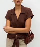 Blusa de manga corta con cuello camisero, abotonadura frontal y detalle de lazo anudado en el bajo. Confeccionada en tejido texturizado con caída fluida.