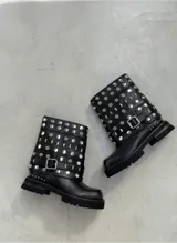 Botas de caña media color negro, con suela track y diseño cargado de tachas metálicas plateadas circulares y rectangulares. Incluye una tira ajustable con hebilla metálica en la zona del tobillo.