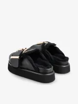 Zueco negro de cuero con plataforma y plantilla recubierta de piel de oveja. Presenta una hebilla dorada de gran tamaño en la capellada.