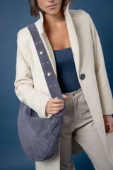 Bolso tipo hobo de gamuza color azul, con correa ancha ajustable decorada con tachas metálicas plateadas.