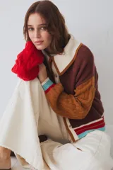 Cardigan de punto multicolor con diseño colorblock, cuello polo rosado con borde rojo, cierre frontal de botones, mangas largas abuchonadas (una roja y otra verde militar con tejido de ochos) y detalles de rayas en los puños y el ruedo.