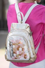 Mochila de cuero blanca y dorada con diseño texturizado tipo cocodrilo y detalles de arte abstracto en tonos nude y rosa. Cuenta con múltiples compartimentos con cierre y herrajes metálicos en oro viejo.