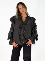Blusa negra de corte holgado con volados en el frente y en las mangas. Presenta detalles de costuras en contraste color blanco en los bordes de los volados y puños elásticos.