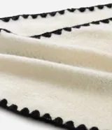 Bufanda de punto color crema con bordes decorados con pespunte en hilo negro. Presenta un diseño rectangular y etiqueta de la marca Accessories.