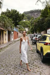 Vestido midi de color blanco con escote en pico y tirantes finos. Presenta un diseño con frunces en la cintura y detalle de lazada frontal.