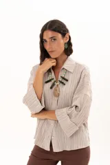 Camisa de textura plisada en color beige, con cuello clásico, cierre frontal de botones y mangas tres cuartos con puños vueltos.