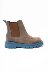 Bota tipo Chelsea de cuero lavado en tono marrón, con paneles laterales elásticos en color marrón oscuro. Presenta una suela track robusta de goma en color azul y un tirador trasero en el mismo tono azul.