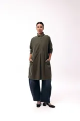 Vestido camisero de silueta amplia y fluida, color verde militar, con cuello camisero, frente abotonado parcial, mangas largas y bolsillos laterales.