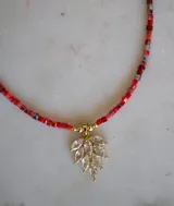 Collar con cadena de pequeños cristales cuadrados en tonos rojos y naranjas, y un dije en forma de hoja con baño de oro y circonitas transparentes.