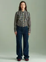 Camisa de viscosa con estampado a cuadros de estilo retro en tonos beige, azul marino, celeste y rojo. Presenta cuello camisero, cierre frontal con botones metálicos plateados y diseño con capas superpuestas en el pecho de inspiración country.