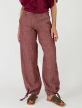 Pantalón de lino color beige, de corte holgado tipo jogger con puños ajustables con cintas en los tobillos, bolsillos laterales y cierre frontal con botón y cremallera.