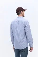 Camisa de manga larga Brooksfield de corte regular, confeccionada en tejido oxford de algodón con estampado de rayas verticales finas en color azul sobre fondo blanco. Presenta cuello abotonado, bolsillo frontal con logo de ave bordado y puños con botones.