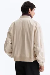 Campera bomber en mezcla de algodón y nylon color beige, con cuello elevado acanalado y cierre frontal de cremallera. Cuenta con bolsillos laterales y un bolsillo con cierre en la manga izquierda. Puños y bajo en punto acanalado, de corte holgado.