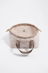 Mini bolso de mano Bimba y Lola con estructura blanda de nylon en color beige. Presenta asas de cinta en tono marrón, cierre mediante cordones laterales amarillos con detalles metálicos y logo metálico frontal.