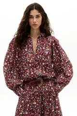 Camisa de lino con estampado floral de margaritas sobre fondo color vino. Presenta cuello camisero clásico, botones frontales de nácar, mangas largas abullonadas y puños con terminación ondulada.