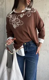 Sweater de punto color chocolate, de corte holgado, manga larga y cuello redondo con delicados bordados contrastantes en el frente.