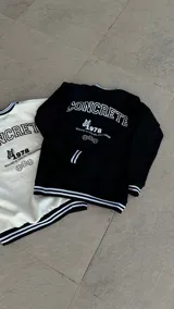 Buzo negro de corte clásico con cuello, puños y ruedo acanalados con doble línea blanca. Estampado frontal con la palabra "CONCRETE" en mayúsculas, una mariposa, el número "1978" y la frase "SOUND & VISUAL PROGRAM".