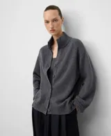 Cárdigan de punto color gris oscuro, confeccionado en lana merino. Presenta cuello alto tipo perkins, manga larga con hombro caído y cierre frontal de botones. Los puños y el ruedo tienen terminación en canalé.