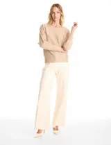 Buzo de tejido fino color beige, con mangas tipo dolman y puños ajustados. Presenta un diseño frontal decorado con apliques de tachas metálicas pequeñas dispuestas en líneas verticales.