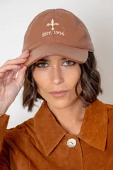 Gorra de cuero color chocolate con visera curva y bordado frontal en hilo color crema que incluye un símbolo y la inscripción 'EST. 1994'.
