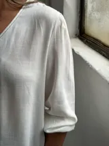 Blusa blanca de manga larga con cuello en V y cierre frontal de botones. Presenta una textura sutil en la tela y un corte recto y holgado.