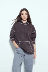 Buzo canguro de calce relajado, color marrón con efecto lavado y costuras a la vista en contraste. Cuenta con capucha integrada y bolsillo frontal tipo canguro.