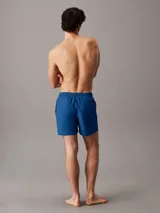 Short de baño de largo medio Calvin Klein, confeccionado en poliéster reciclado de secado rápido. Presenta cintura elástica con cordón ajustable, forro de malla interior, bolsillos laterales y un bolsillo trasero. Destaca por el logo de la marca estampado en vertical sobre la pierna.