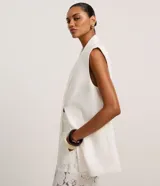 Chaleco largo de sastrería color blanco, con solapas tipo peaked, cierre frontal oculto y ajuste mediante lazo con hebilla en la espalda.