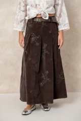 Pollera larga de pana color chocolate, con diseño de tablas frontales y bordados florales en tono contrastante. Cuenta con presillas para cinturón.