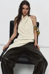 Top color crema confeccionado en viscosa, con cuello halter drapeado, espalda descubierta y bajo asimétrico. Cierre en el cuello con botón.