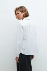 Camisa blanca de manga larga con cuello clásico y cierre frontal con botones.