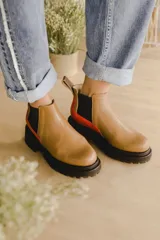 Botas estilo Chelsea en color tostado, con paneles laterales elásticos negros, suela chunky negra de goma y un detalle de tira roja en el talón.