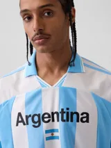 Camiseta de fútbol estilo retro de la selección argentina, con diseño de rayas verticales blancas y celestes. Presenta cuello polo, mangas cortas y el texto 'Argentina' estampado en el pecho junto a una pequeña bandera nacional. Incluye etiqueta oficial de FIFA Classics en el ruedo.