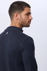 Buzo tejido de punto con textura en relieve, color azul marino. Presenta cuello alto con cierre frontal parcial y detalles en gamuza en la zona del cierre. Posee puños y ruedo acanalados.