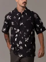 Camisa de manga corta Calvin Klein con corte relaxed fit, confeccionada en algodón regenerativo. Presenta un estampado floral en tonos blanco y gris sobre fondo negro, cierre frontal con botones y un bolsillo de parche en el pecho con el logo de la marca bordado.