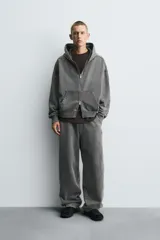 Sudadera con capucha y cierre de cremallera, de corte relajado (relaxed fit), confeccionada en algodón con interior afelpado. Presenta bolsillos frontales tipo canguro y acabados en rib. El tejido tiene un efecto lavado que le da un color negro desgastado.