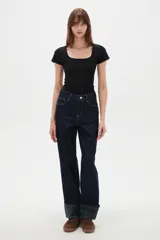 Pantalón de jean azul oscuro de corte recto y tiro alto, con costuras en contraste y dobladillo con vuelta que revela un estampado de cuadros en tonos verdes y azules.