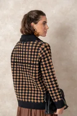 Chaqueta de punto grueso con patrón geométrico de cuadros en blanco y negro. Presenta cuello camisero, cierre frontal con cremallera y tirador circular, bolsillos frontales y puños acanalados.